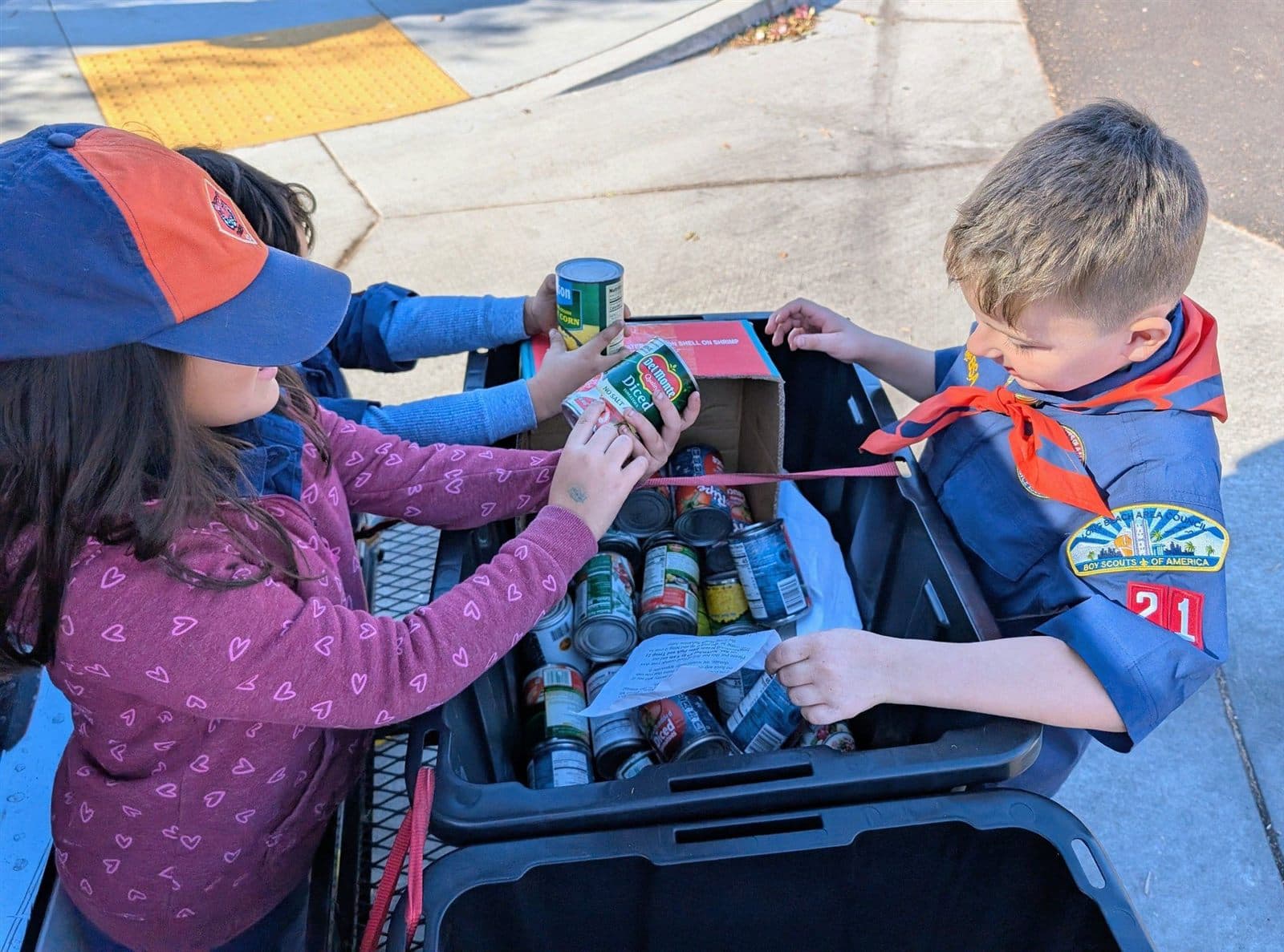 Cub Scouts loading canned food into a collection wagon on the sidewalk